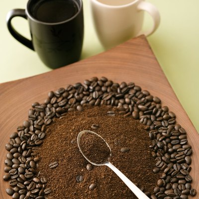 Spoon in pile of ground coffee and whole beans with mugs
