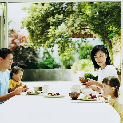 Family of Four Dining at a Table With French Windows Open Onto a Courtyard