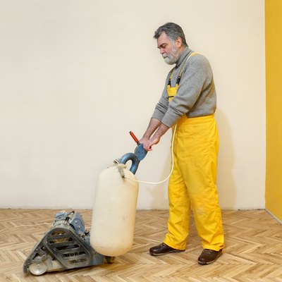 Worker polishing old parquet floor with grinding machine