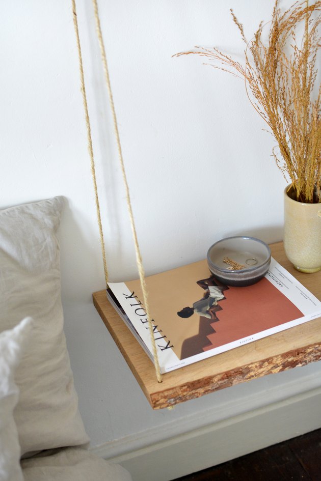 Étagère en bois suspendue à une corde avec un magazine et un bol gris et un vase beige.