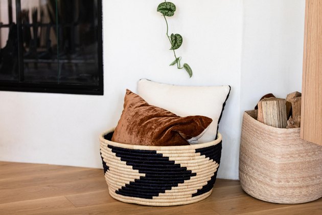 basket with two throw pillows next to a fireplace on a hardwood floor