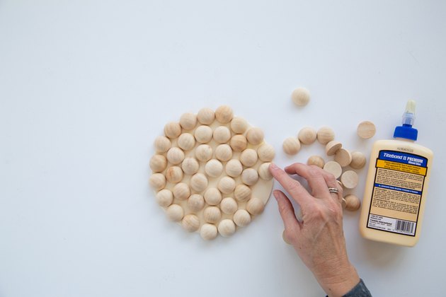 Ajouter des perles de bois fendues à un cercle de bois en utilisant de la colle pour faire un dessous de plat moderne.