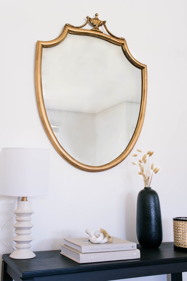 DIY antique gilt mirror hanging on wall above black table with lamp, books, and vases