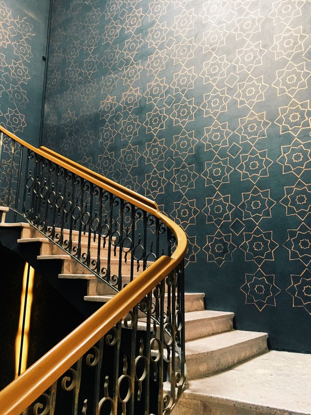 Gold and black painted stair rails with blue wallpaper.