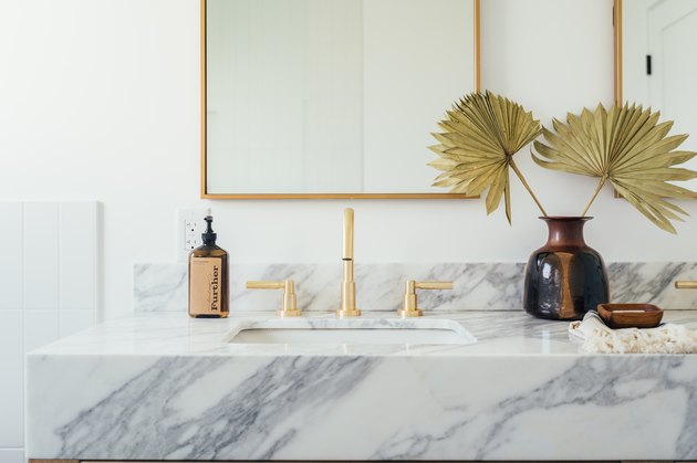 stone bathroom vanity, brass faucet in front of a rectangular mirror with gold trim