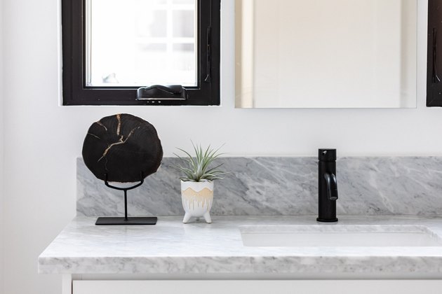 quartz bathroom countertop, black faucet, white vase with green plant, black decorative stand