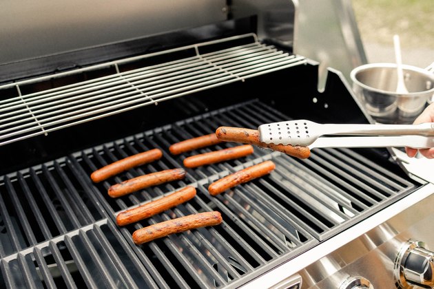 Close-up of hot dogs on grill and using tongs to turn one over