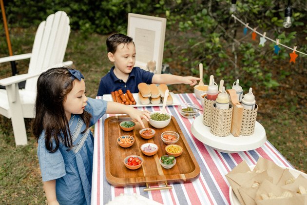 Two small kids pointing to toppings on the hot dog bar table