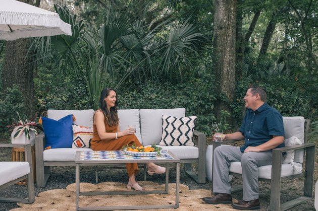 Woman and man sitting in outdoor patio with DIY tiled coffee table, colorful pillows and fringe umbrella