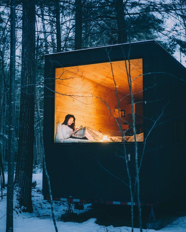 Girl reading in tiny snow-surrounded cabin.