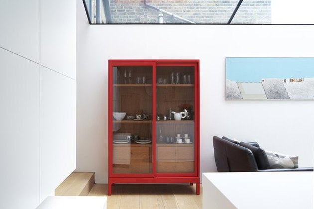 White modern room with large skylight, painting, light wood floors and vermillion color display cabinet with glass doors.