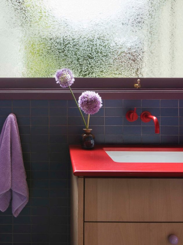 vermillion color counter, red faucet, purple window trim, towel and flowers, blue tile.