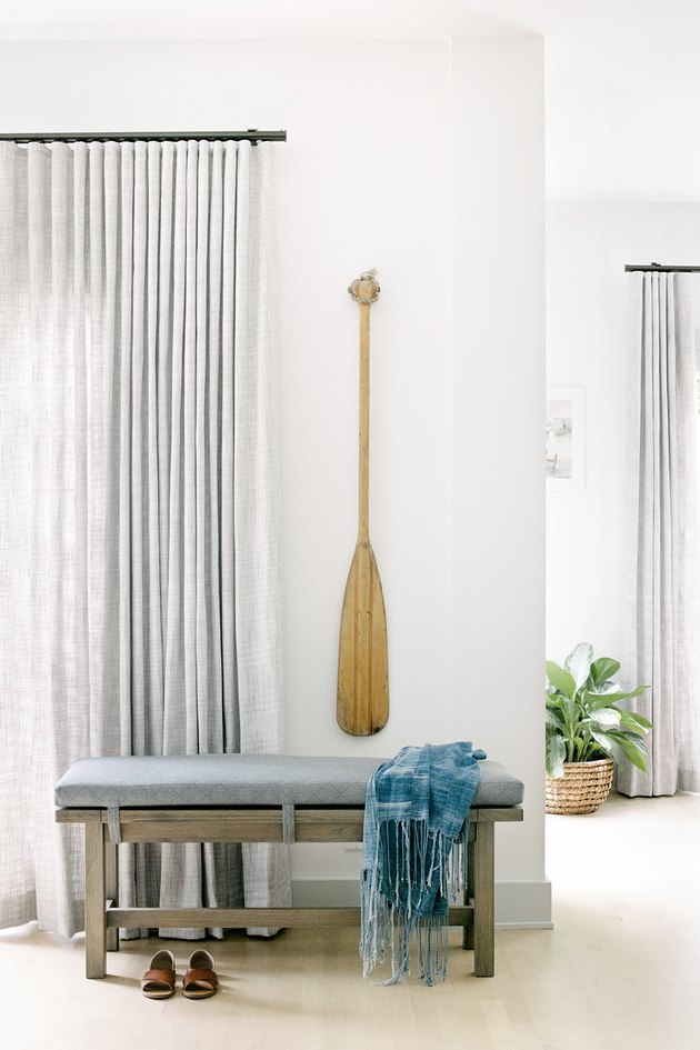 Vintage oar hung on white wall above accent bench