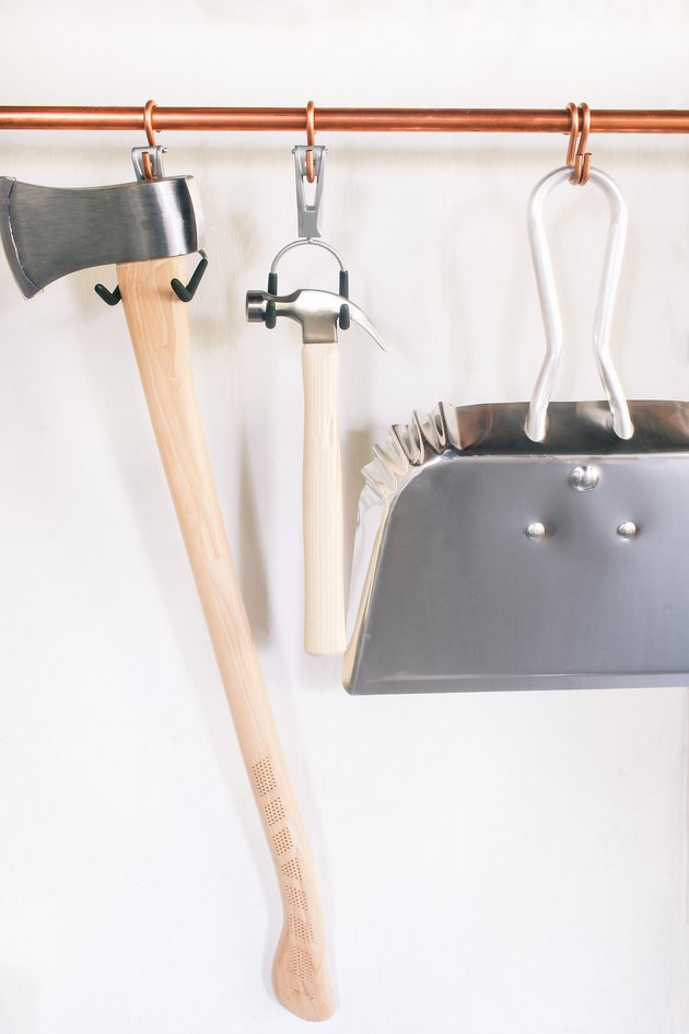 Axe, hammer and dustpan hung on copper pipe with utility hooks