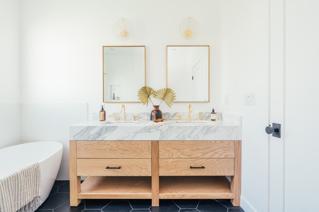 Bathroom with square brass mirrors, sconces, wood and marble sink, and tub