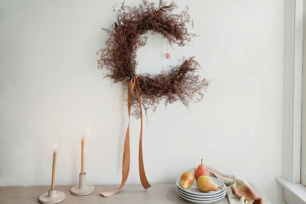 DIY crescent moon shaped dried floral wreath on wall above table with pears, plates and candles
