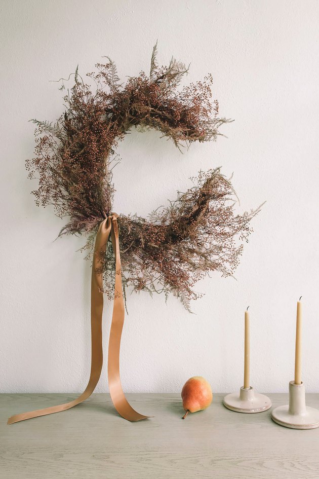 DIY crescent moon wreath with dried florals hung on wall above table with candles and pear