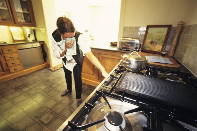 Woman in kitchen, turning off gas cooker, towel to face