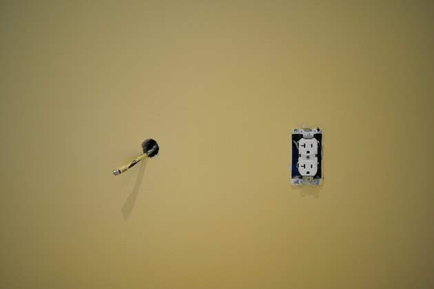 Coaxial cable hanging out of freshly painted wall next to an electric outlet 3 prong plug during renovation and construction