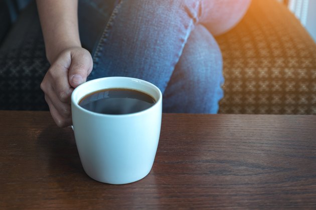 Closeup image of a woman's hand holding a cup of hot coffee to drink while sitting in cafe