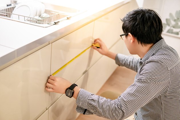 Asian man using tape measure on kitchen counter