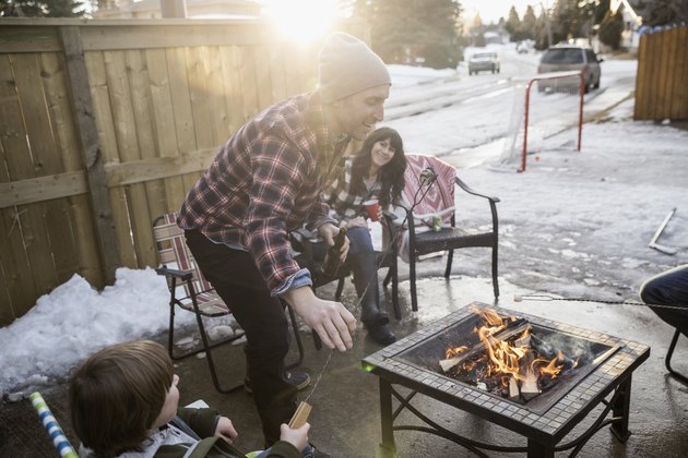 Family roasting marshmallows at fire pit in snowy driveway