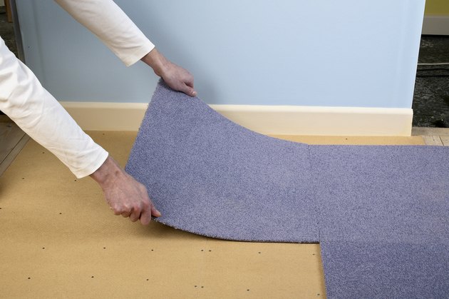 Man installing carpet tiles on top of hardboard floor