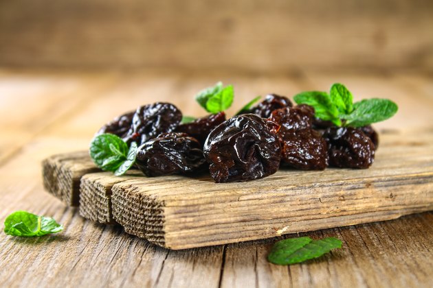 Prunes with mint leaves in a bowl on an old wooden table.