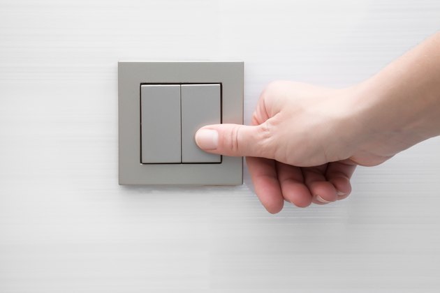 Woman's hand pressing light switch at the wall.