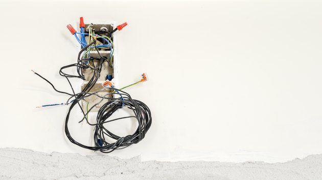 Circuit breakers and fuses in a plastic box on a wall with wires hanging out and unplugged