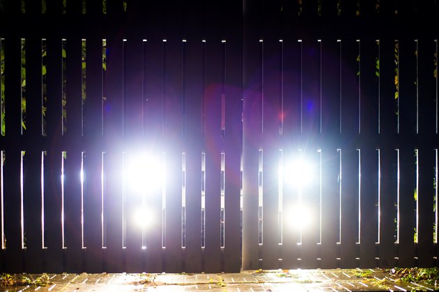 The car stands on the territory of the house at night. Light headlights through the fence