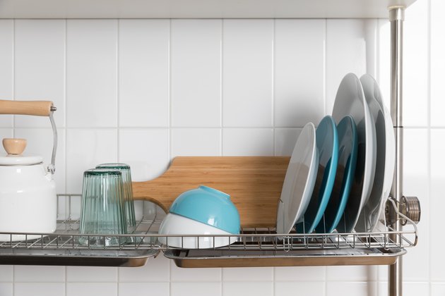 Clean dishes drying on metal dish rack on light background. Kitchen utensils and dishware on wooden shelf. Kitchen interior background.Text space.