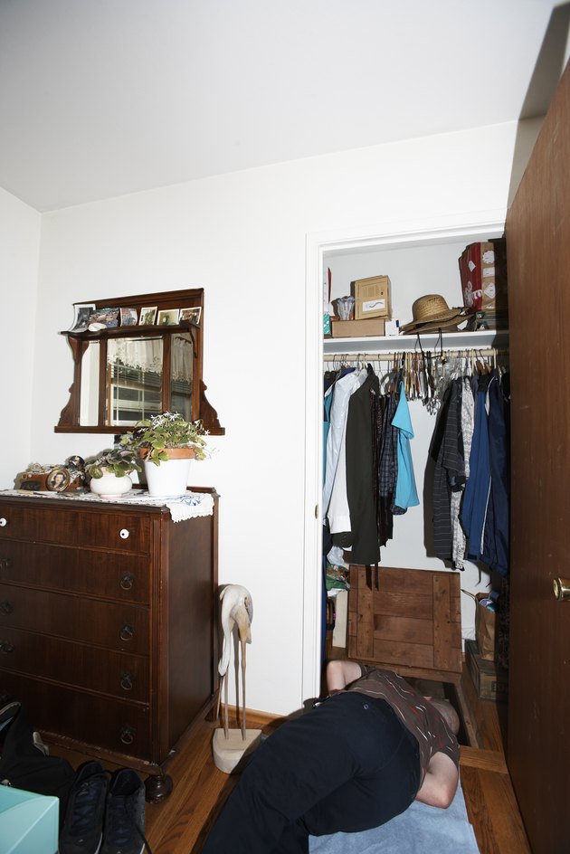 Young man lying on floor, looking down into crawl space in closet
