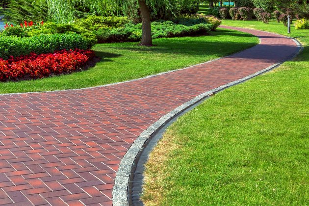 Red blocks footpath with drainage system in a park with green lawns and landscape design with bushes and red flowers.
