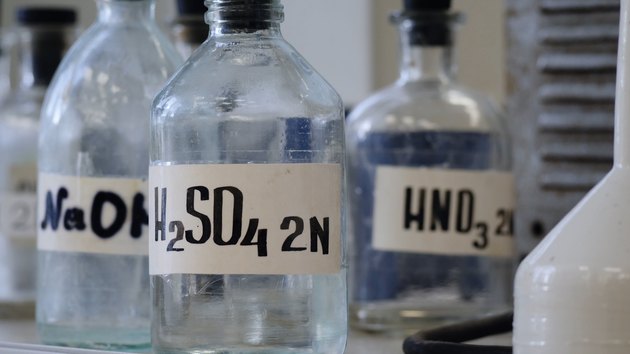 Bottles of solutions stored on shelf in laboratory. Bottles with chemical solutions of NaOH, H2so4 and HNO3. Sulfuric acid, sodium hydroxide, nitric acid