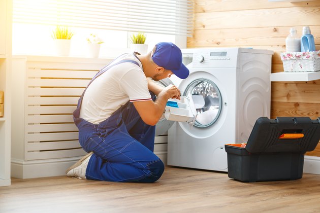 working man plumber repairs washing machine in laundry