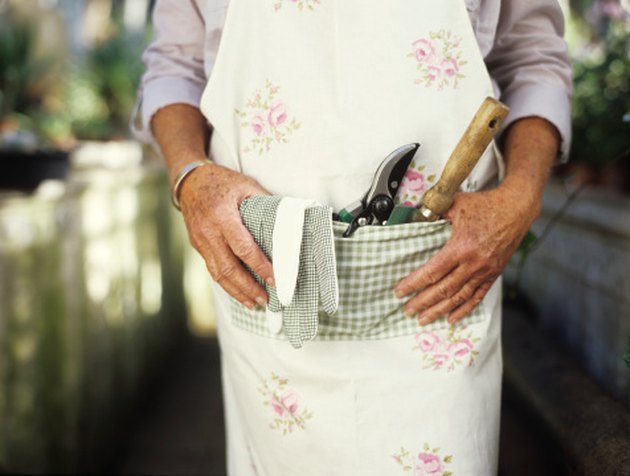 Senior woman with gardening tools in pocket of apron, mid section