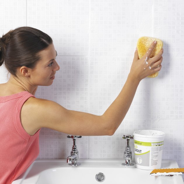 Woman cleaning tile wall in bathroom