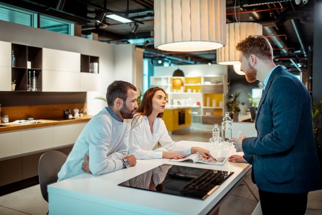 Young husband and wife getting informed about a kitchen appliance from a brochure with assistance from a store employee