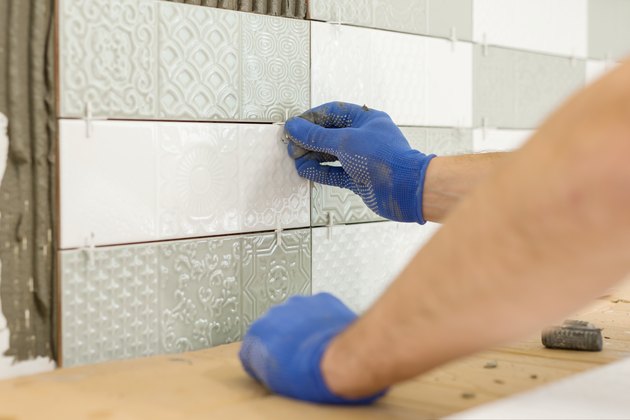 Installing ceramic tiles on the wall in kitchen. Placing tile spacers with hands, renovation, repair, construction.