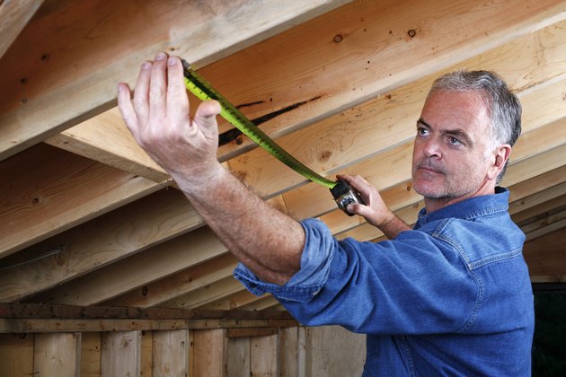 Man measuring distance between rafter beams of home addition.