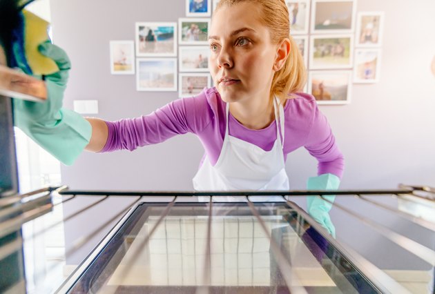 Young woman in white apron cleaning oven