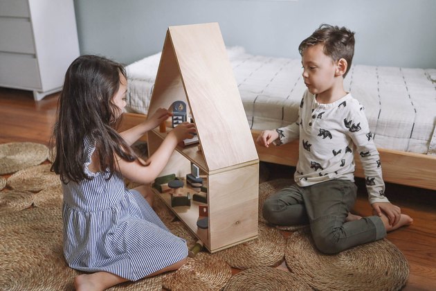 Petite fille et garçon jouant avec maison de poupée