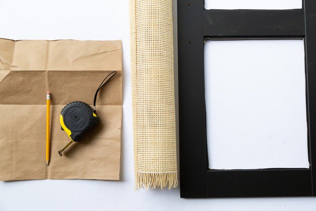 Brown paper with pencil and measuring tape, next to caning and black IKEA cabinet