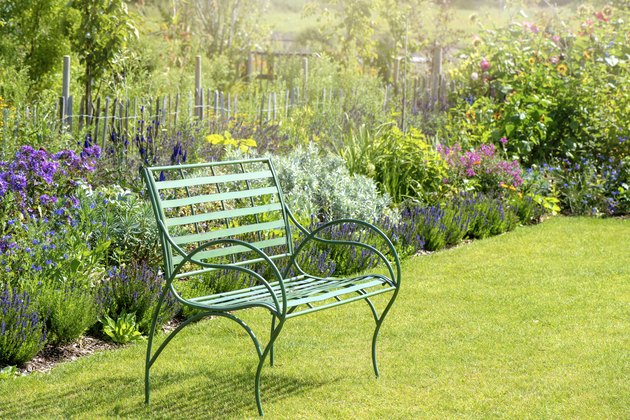 Close-up image of a wrought iron, green garden seat by a summer herbaceous border