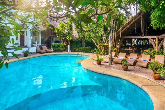Beautiful tropical resort swimming pool with vibrant turquoise water, surrounded by lush, tropical vegetation and resort buildings.