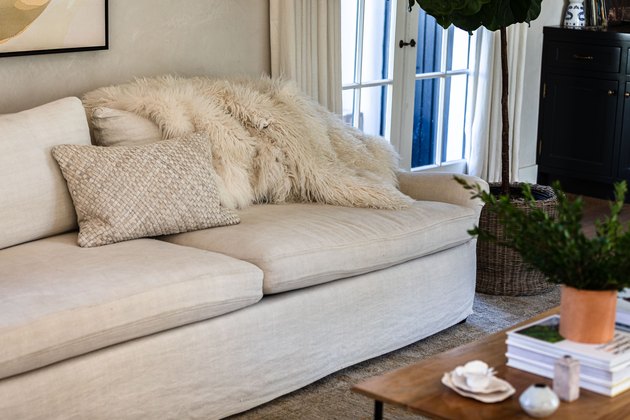 Un canapé de salon blanc avec oreiller assorti et une couverture en fourrure blanche près d'une table basse