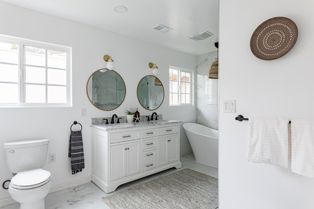 Minimalist white bathroom with large round mirrors, windows and gray rug