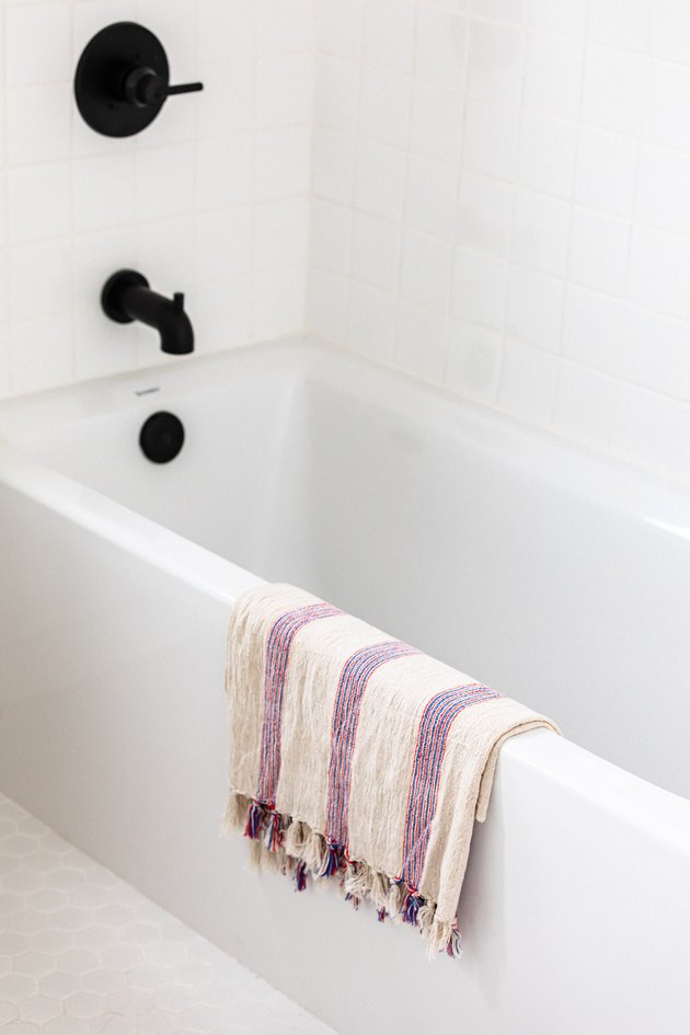 White bathtub with black faucet and handle with white and purple towel hanging on the tub in white room
