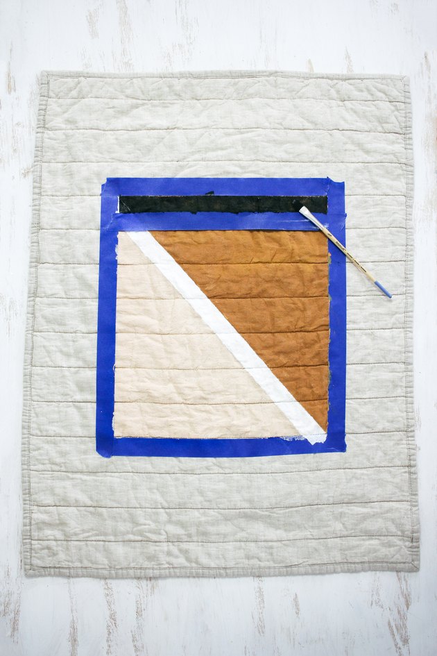 Quilted pillow shame with blue painters tape around brown, black and white design